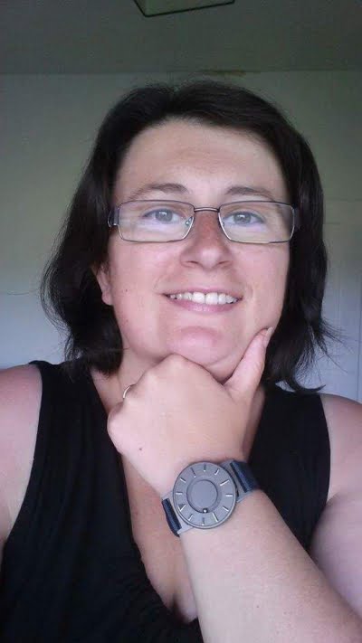 Dark haired lady wearing a grey Bradley tactile watch, she has her hand on her chin and is smiling.
