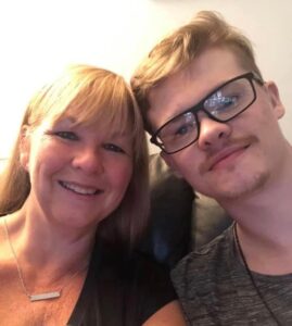 Mum and son, smiling and looking at the camera, son wearing glasses and looking forward.