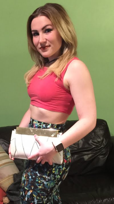 Young lady wearing an orange crop top, patterned skirt and holding a cream clutch bag.