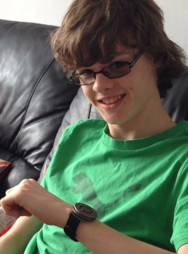 Young boy wearing a green t-shirt, he is wearing dark glasses and a smile. On his left wrist he is wearing a Bradley tactile watch.