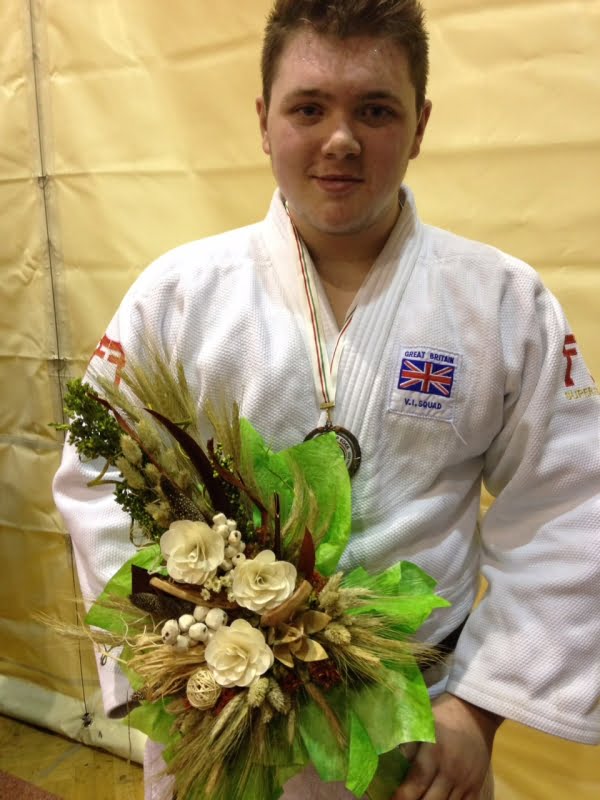 Jack Hodgson wearing his judo kit and a medal along with a bouquet of flowers.