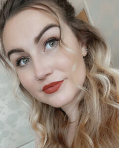 Close up of Molly Watt, with red lipstick, looking thoughtfully up to the top right hand corner of the photo.